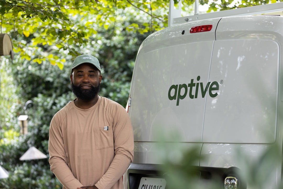 Aptive Pest Control Specialist Standing And Smiling In Front Of An Aptive Van.